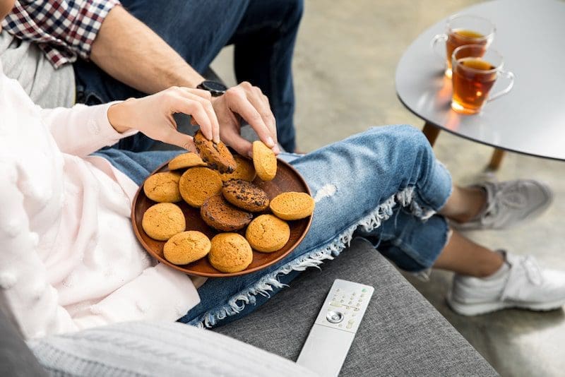 couple eating biscuits and drinking tea on couch