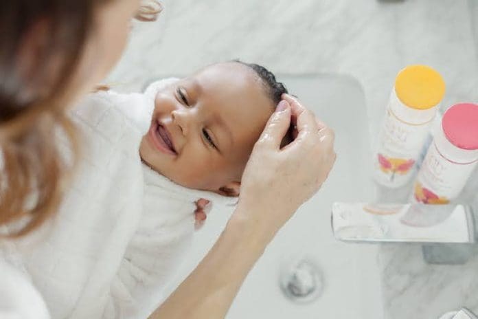 woman washing newborn baby wrapped in white towel - East End Taste Magazine