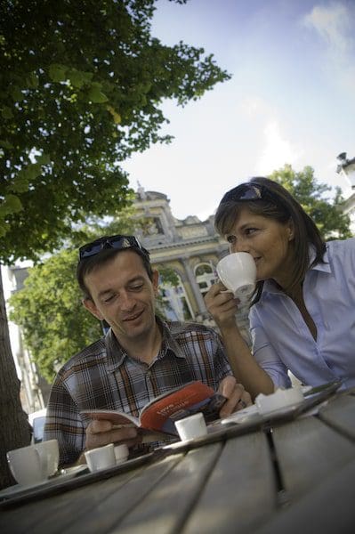 couple drinking coffee and reading travel book outside