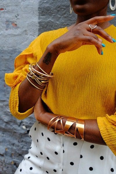 woman with sunflower colored sweater with bangles bracelets blue nail polish