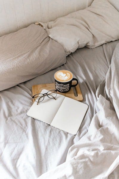 coffee with book on unmade bed sheets latte