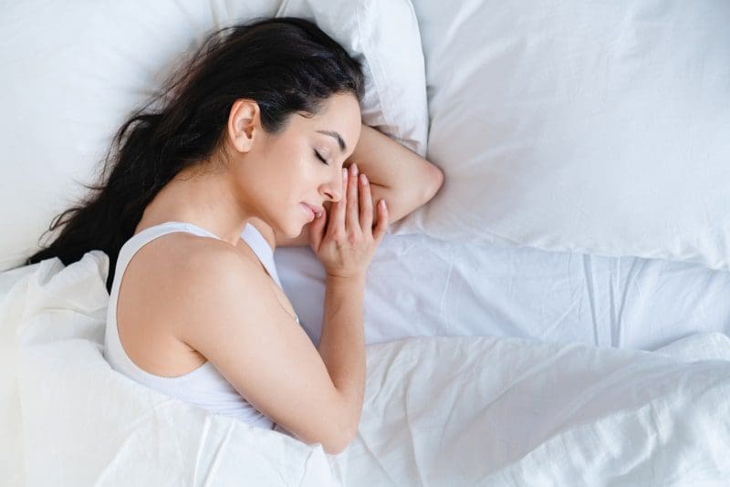woman with dark brown hair sleeping in white sheets and pillow