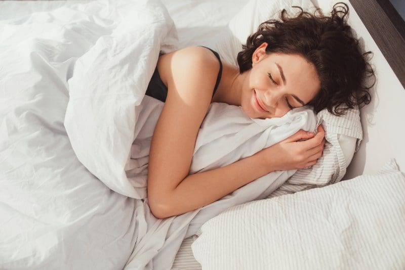 woman with dark hair sleeping in white sheets