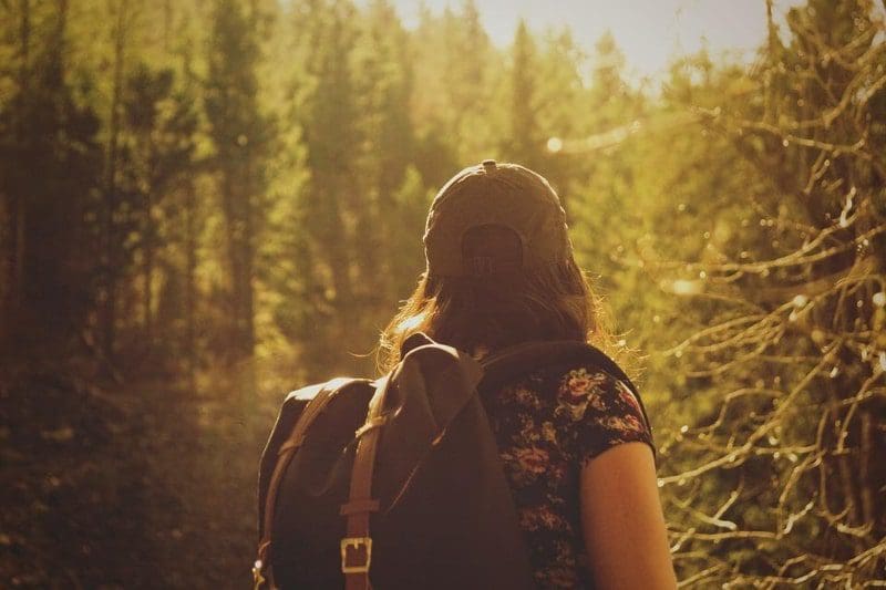 woman in sunlight forest hiking with baseball cap backpack