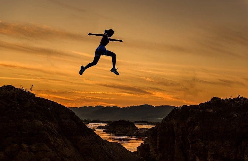 woman jumping across mountains in sunset