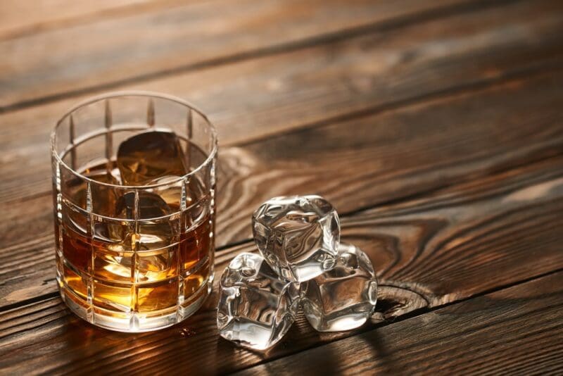 bourbon in a glass with ice and ice cubes on the side wooden table