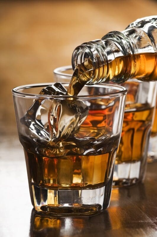 bourbon whiskey being poured into a glass with ice