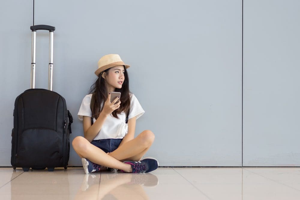 woman looking at her phone wearing hat black luggage airport