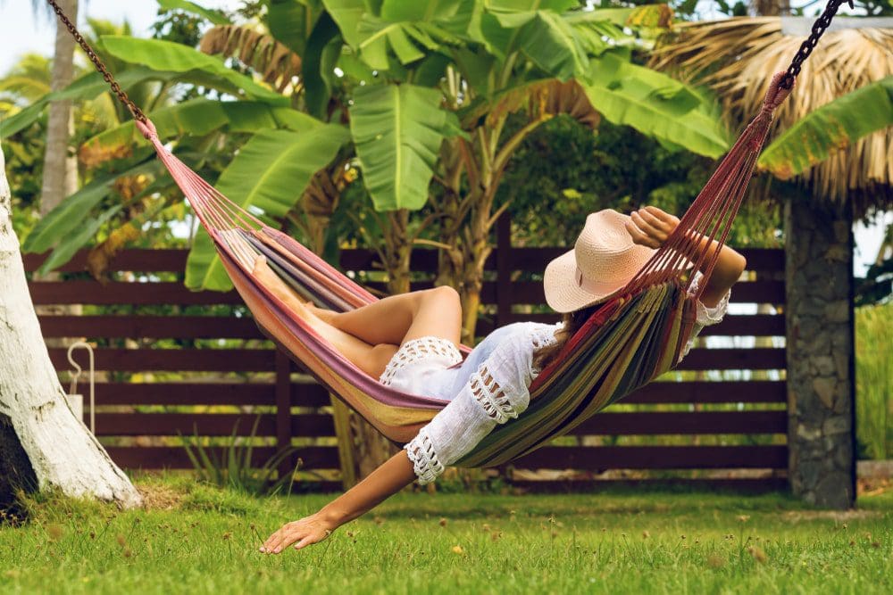 woman relaxing on a hammock at home resort with hat green grass
