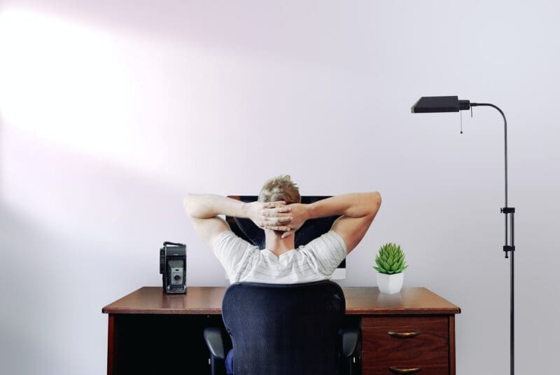 man working at desk hands behind head