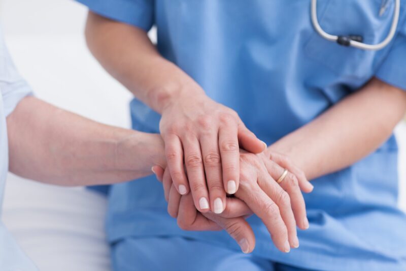 woman nurse holding elderly patient's hand care scrubs
