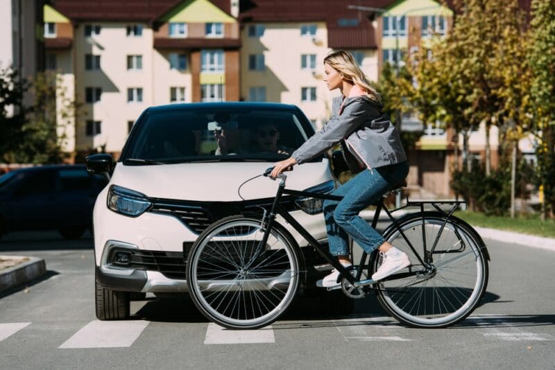 Woman riding bicycle while crossing road with white car