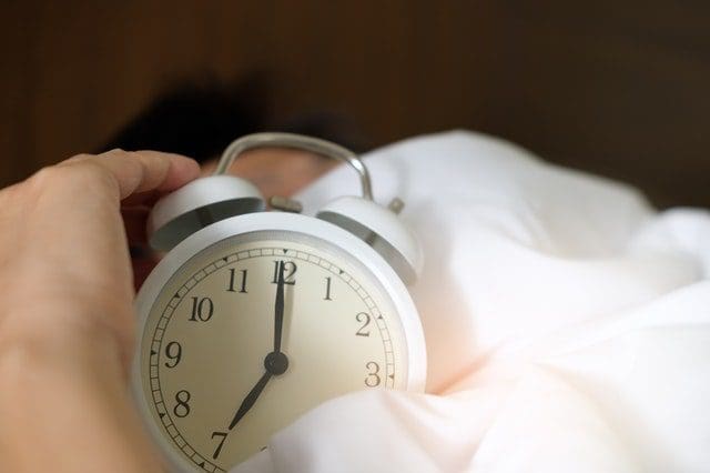 person holding alarm clock on bed