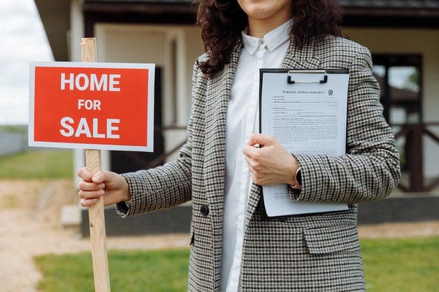 close up of a woman holding a home for sale sign