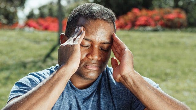 man rubbing head headache outside sitting down