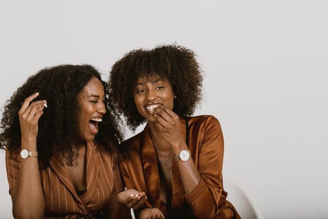 two women with curly hair laughing together wearing brown jackets