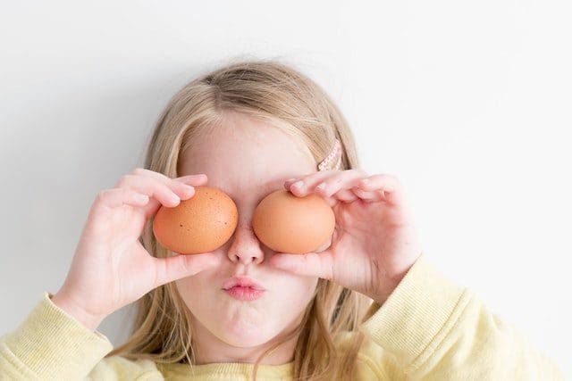 young girl with blonde hair holding brown eggs over eyes