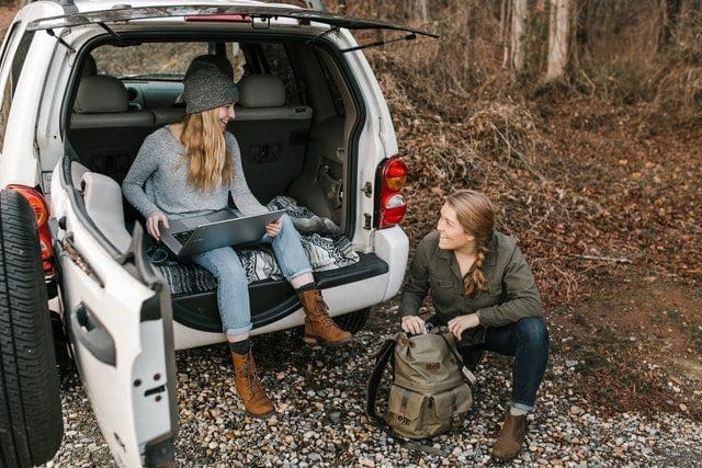 woman in gray coat sitting on white car with friend