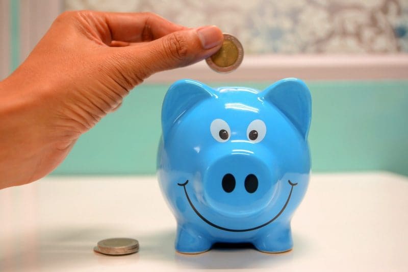 person putting coins inside blue piggy bank