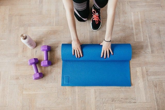 sportswoman unfolding yoga mat on wooden floor