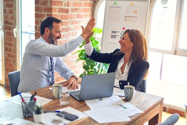 Two middle age business workers smiling happy and confident. Working together with smile on face hand giving high five at the office