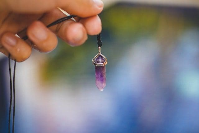 Person Holding Black Necklace With Purple Stone Pendant