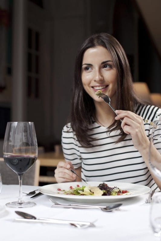 Woman eating dinner white tablecloth glass of red wine