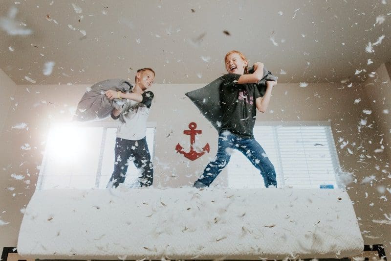 two children throwing pillows feathers around bedroom