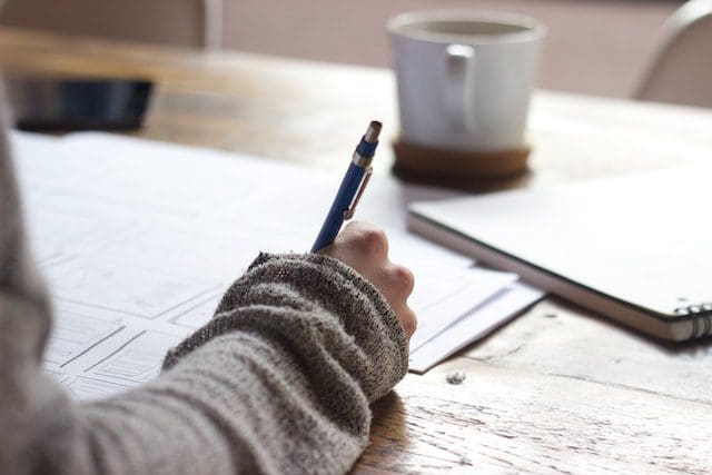 person with grey sweater sleeve writing with pen mug