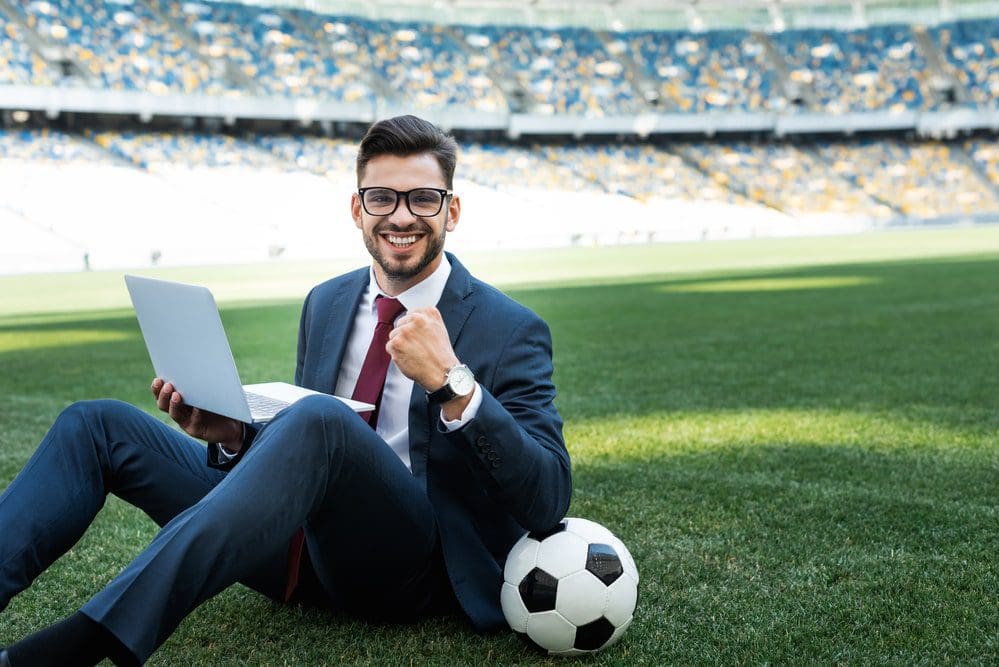 Smiling young businessman in suit with laptop and soccer ball