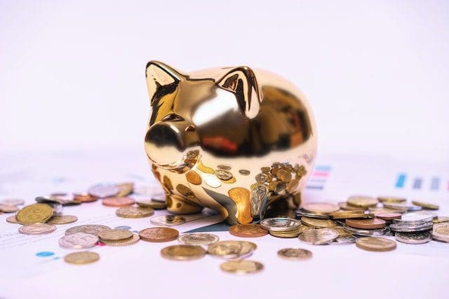 gold piggy bank surrounded by coins white surface