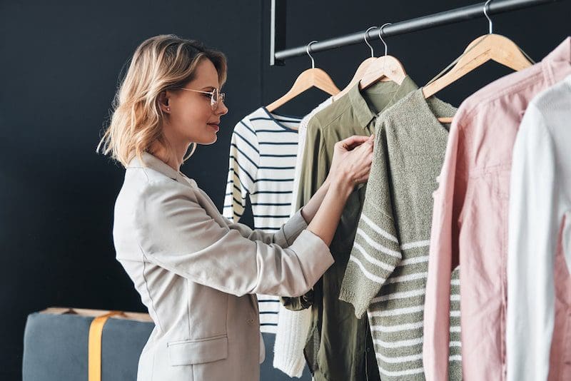 Blonde woman choosing clothes from rank while standing