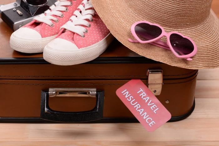 Suitcase and tourist stuff with inscription travel insurance on wood