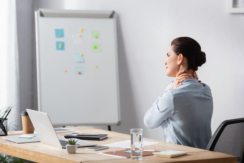 Brunette businesswoman with hurting neck sitting on office chair