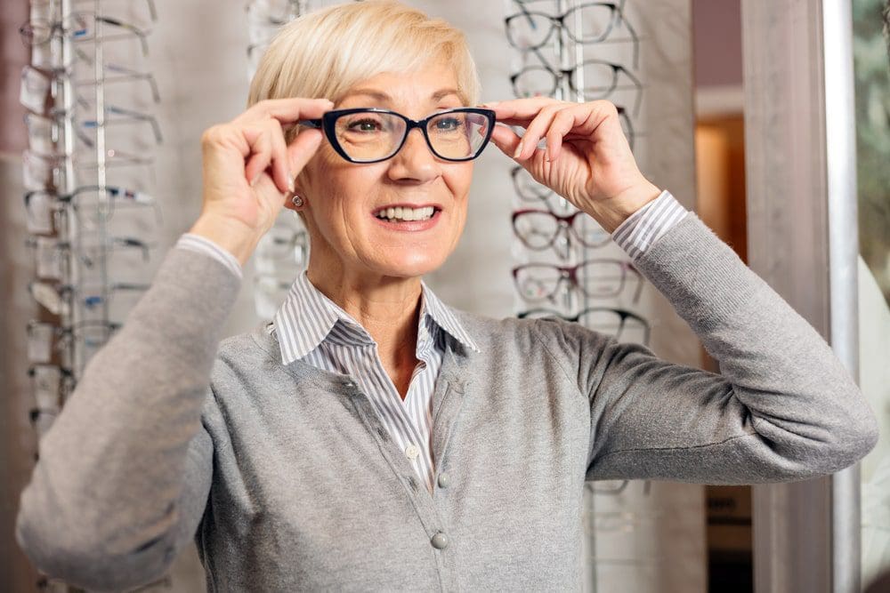 Smiling senior woman trying prescription glasses in optician store