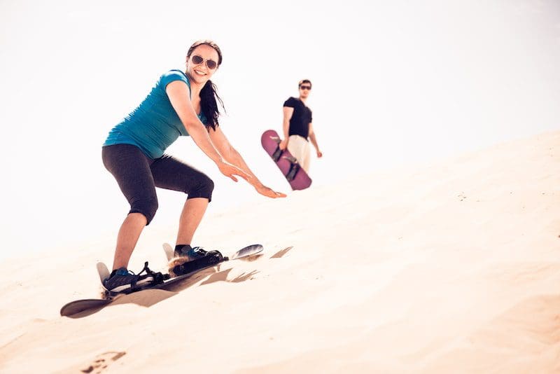 Tourist Sandboarding In The Desert