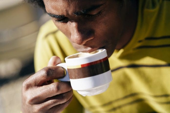 Black man enjoying coffee in cafe while sitting at the table outdoors
