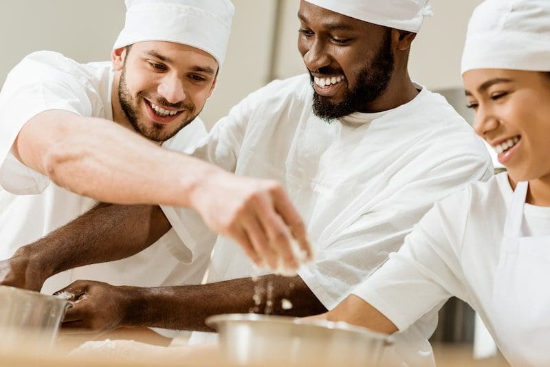 Laughing group of baking manufacture workers kneading dough