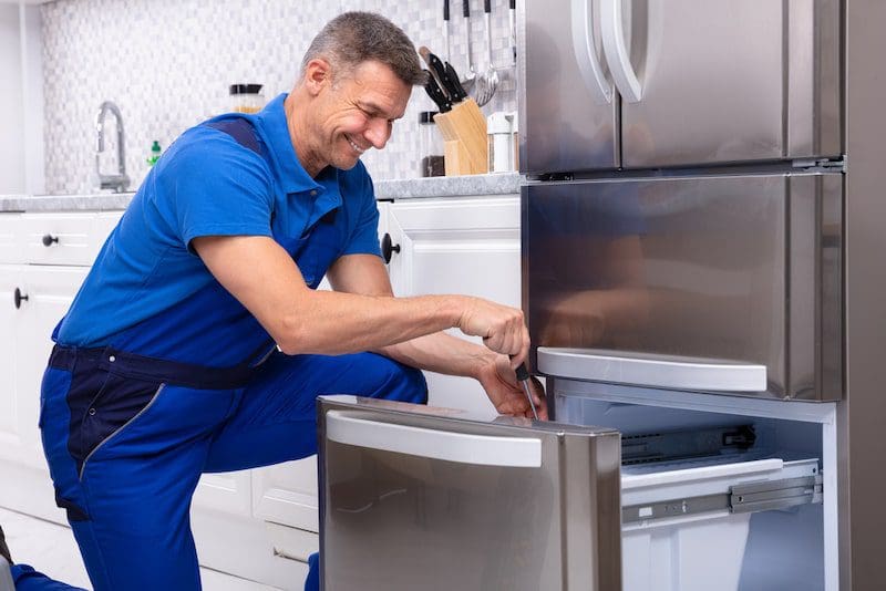 Mature Male Serviceman Repairing Refrigerator With Toolbox