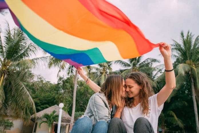 Two women with rainbow flag on the beach on a background