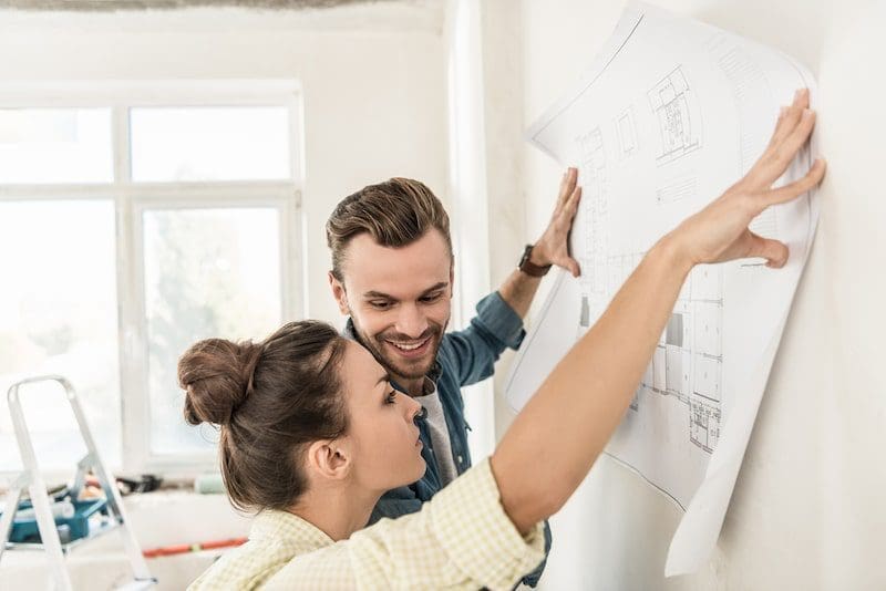 Young couple holding blueprint at wall during renovation