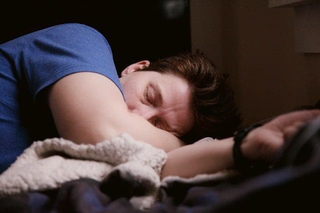 man with brown hair in blue shirt lying on bed