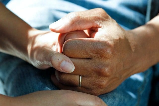 person wearing gold wedding band clasping hands