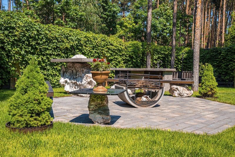Beautiful sunny backyard with iron fire pit and bench on stone pavement