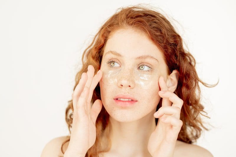 Young freckled woman applying protective or hydrating face