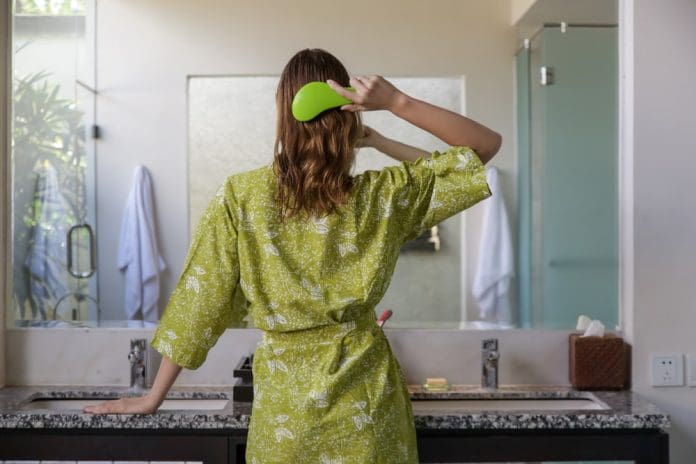 Hair care. Rare view of brunette woman combing hair with green brush