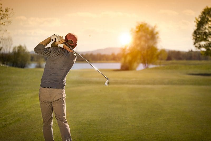 Male golf player swinging golf club at dusk
