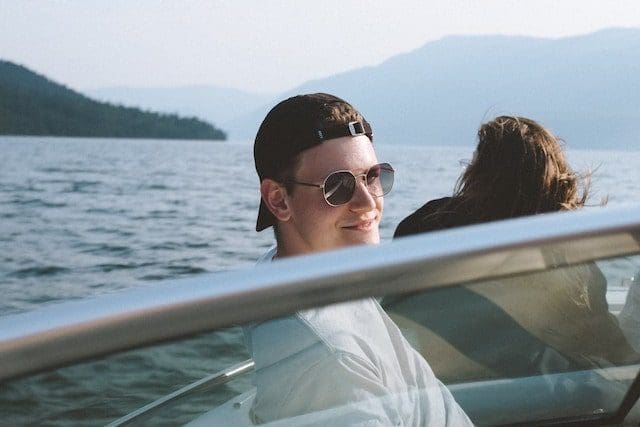 man on motorboat sunglasses baseball hat smiling