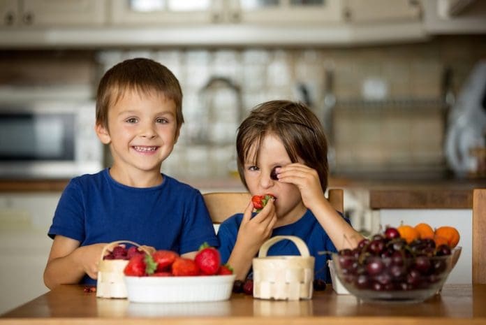 Two sweet children, boy brothers, eating fresh fruits at home