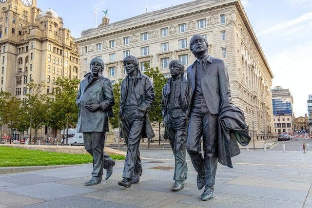 the Beatles statue black coats standing near white concrete building during daytime